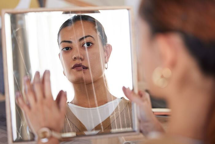 Kvinne som ser på sitt eige ansikt i ein knust spegel
